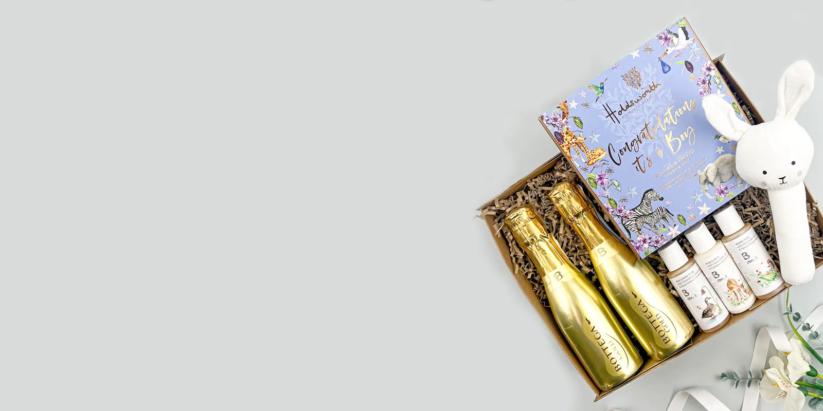 Luxury new baby gift hamper with champagne bottles, baby skincare set, soft bunny toy, and keepsake book in a presentation box