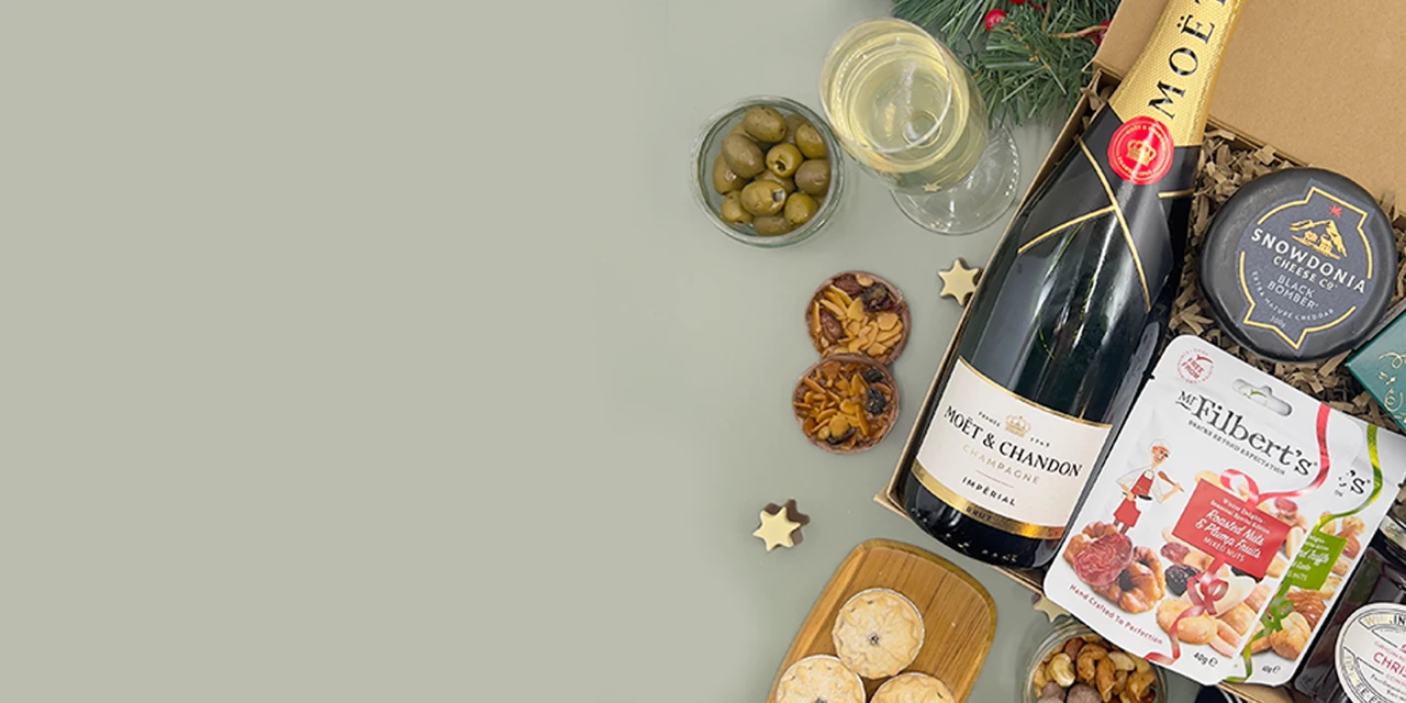 Luxury Christmas food hamper with champagne, gourmet snacks, olives, artisan crackers and festive treats beautifully arranged on a soft sage green background.