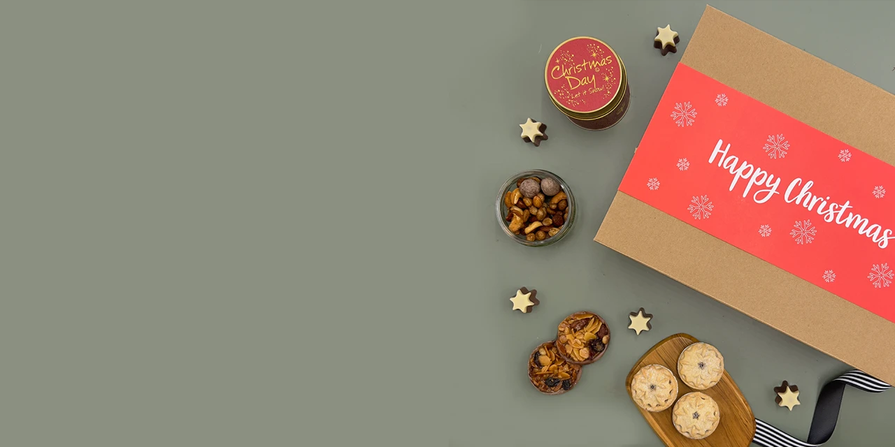 Luxury Christmas food hamper with champagne, gourmet snacks, olives, artisan crackers and festive treats beautifully arranged on a soft sage green background.