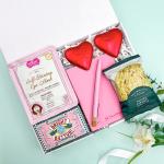 Bright as a Button letterbox gift box with chocolate button bar, self-heating eye mask, pink A6 notebook, matching pink pen, two foil-wrapped chocolate hearts, and salted caramel biscuits in a white gift box.