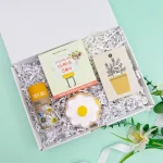 Thank you letterbox gift box with Daisy Daisy wildflower seeds, a thank you milk chocolate bar, a daisy-shaped iced biscuit, and a mini plant-themed thank you card, presented in a white gift box with shredded paper filling.