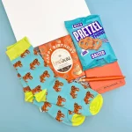 Men’s birthday letterbox gift featuring tiger-print socks, birthday chocolate, salted pretzel thins, an orange notebook, and matching pen in a gift box.