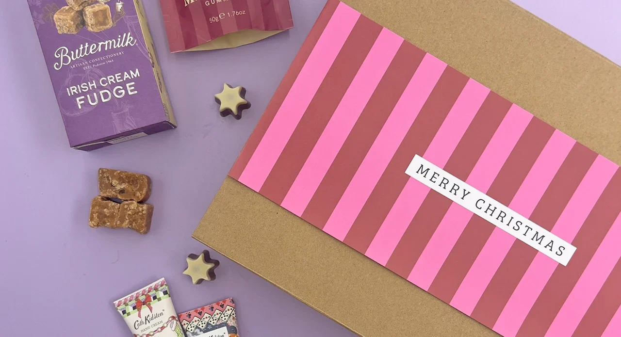 Build your own Christmas hamper for her with luxury fudge, festive chocolates, beauty treats and a pink striped Merry Christmas gift box on a soft lilac background.